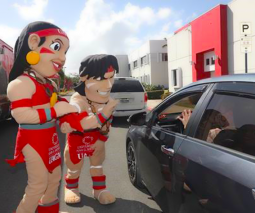 Imagen del taíno y la taína, las mascotas de la UAGM, saludando a un carro que está pasando