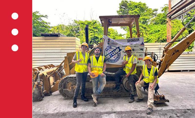 grupo de estudiantes vestidos de trabajadores con excavadora al fondo
