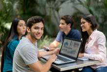 Grupo de estudiantes sentados en mesa en un patio mirando una computadora