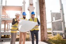 3 ingenieros parados frente a una construcción mirando un plano